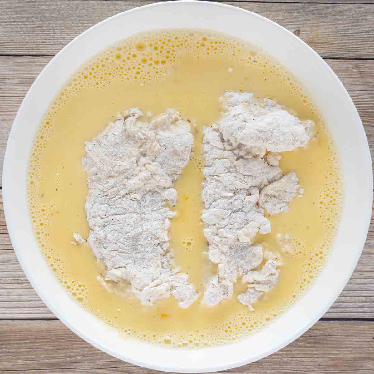 floured chicken tenders in a white bowl with egg wash