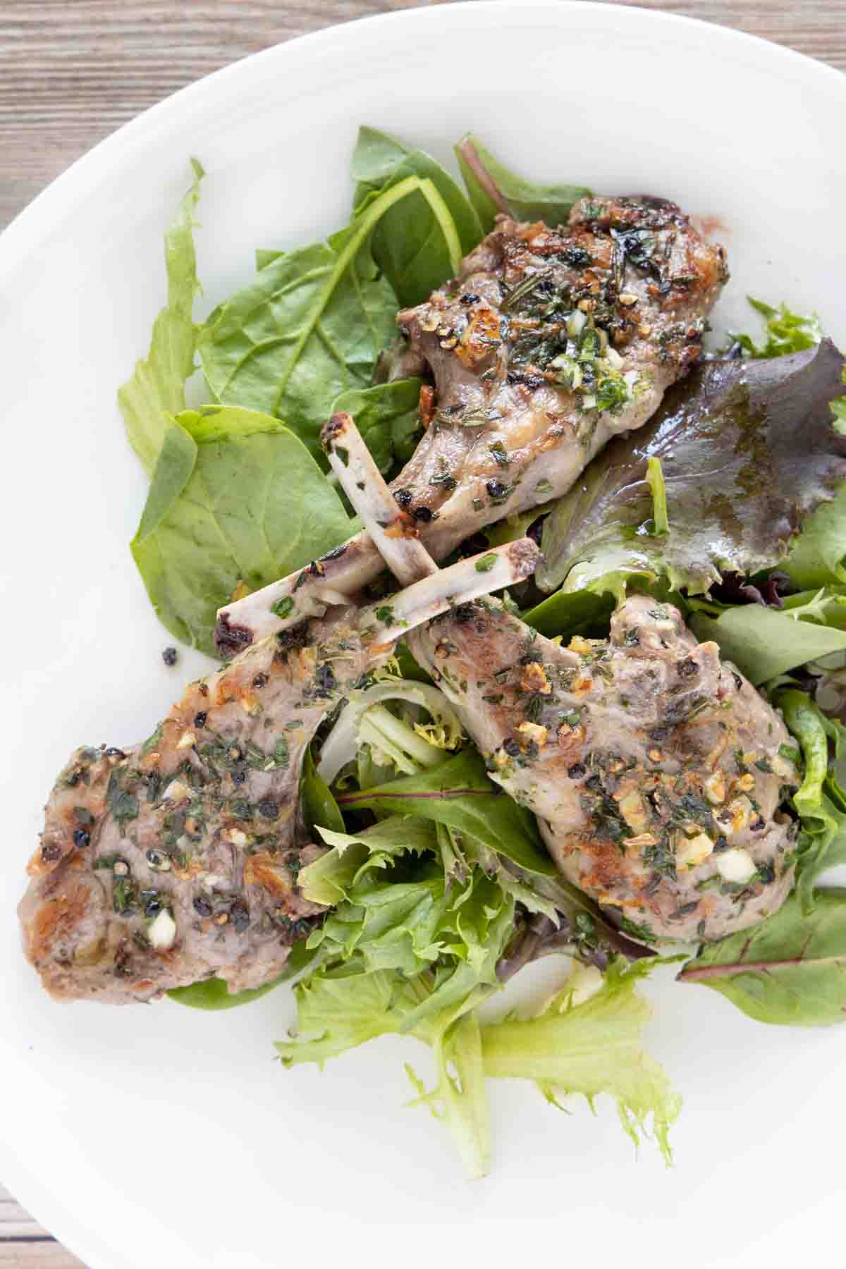 garlic herb lamb chops on a bed of greens on a white plate.