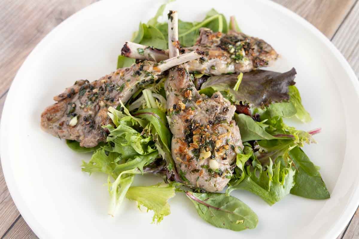 garlic herb lamb chops on a bed of greens on a white plate.