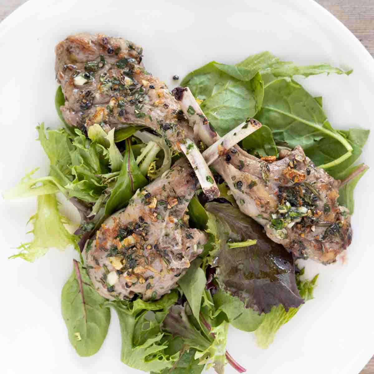 garlic herb lamb chops on a bed of greens on a white plate.