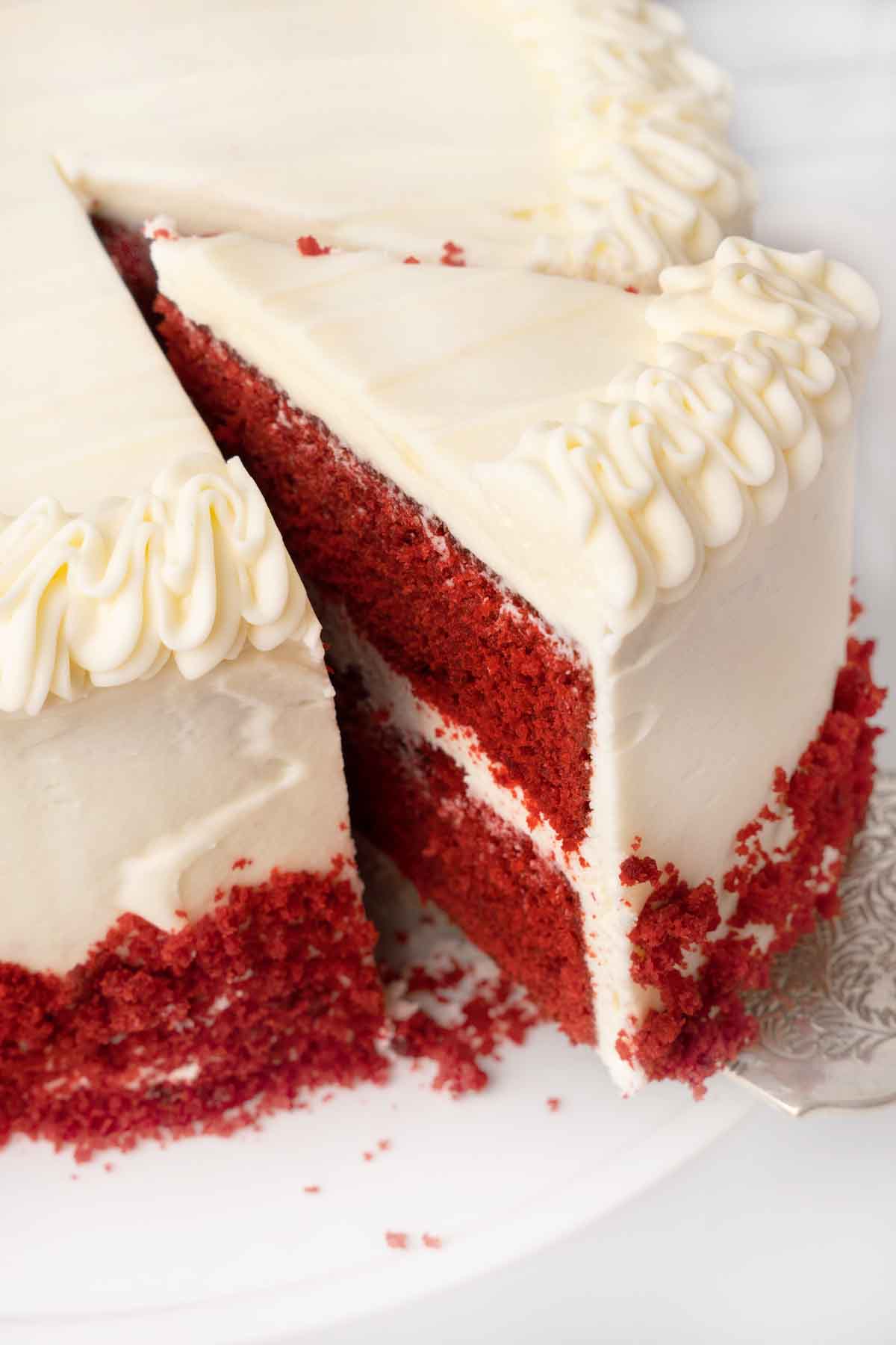 slice of red velvet cake on a spatula being  taken out of whole cake.