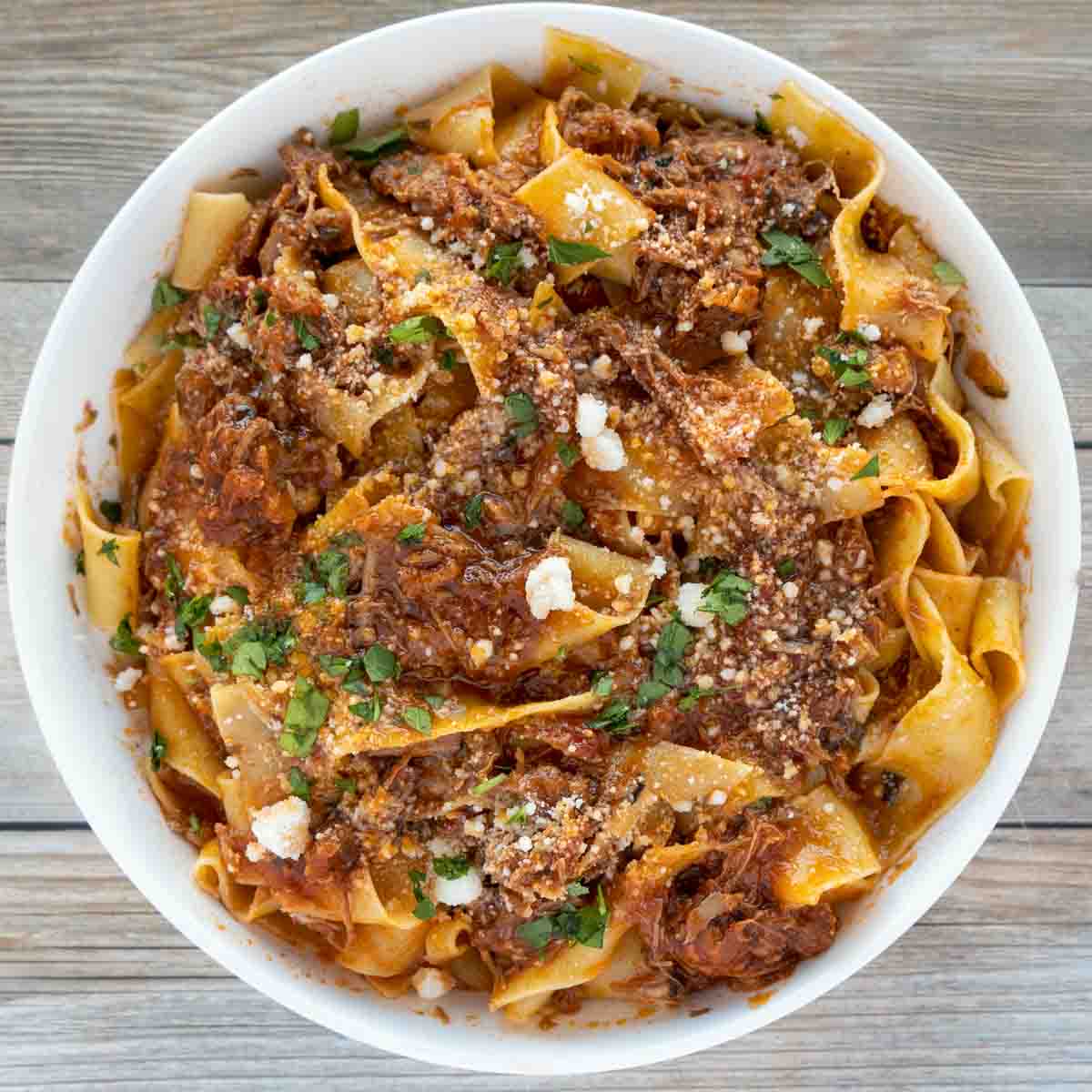 overhead view of ragu napoletano over pappardelle in white bowl 