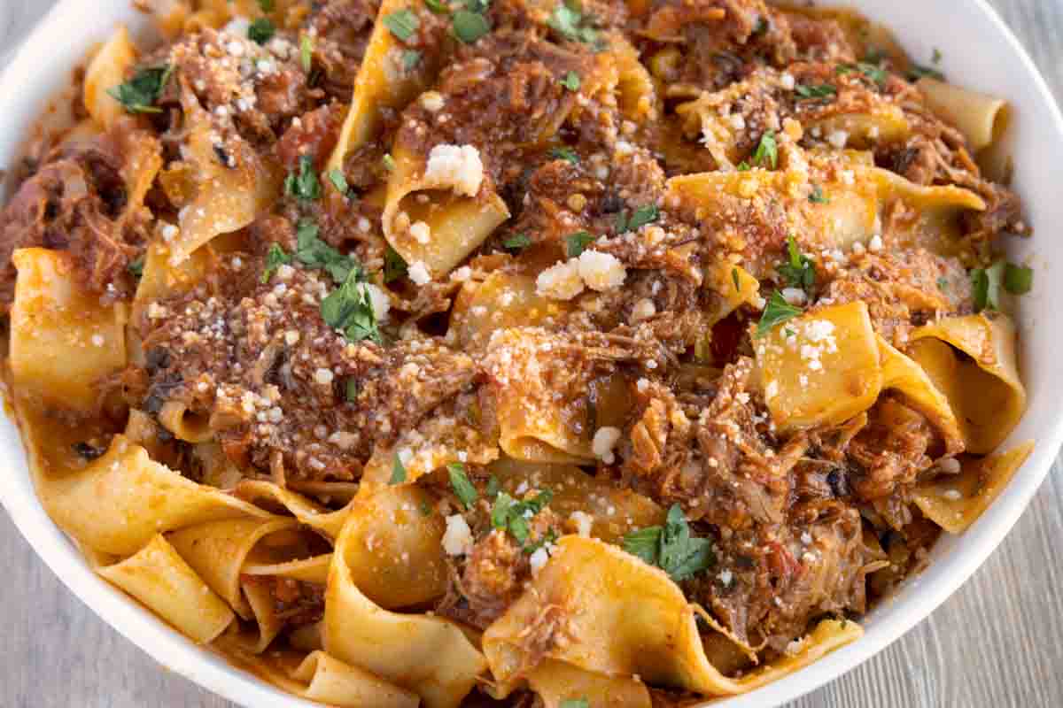 close up of  ragu napoletano over pappardelle in white bowl 