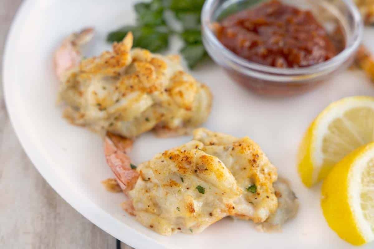 close up of crab stuffed shrimp on a white plate with cocktail sauce and lemons