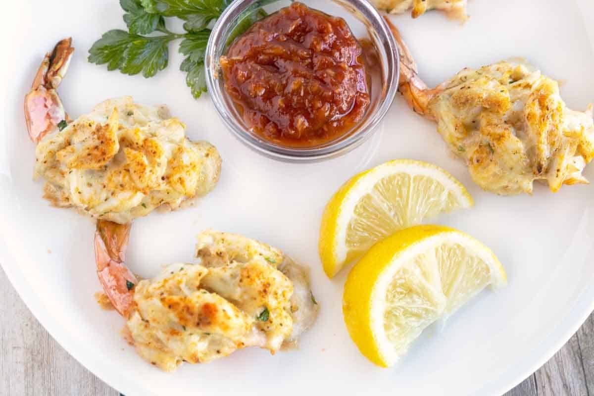 baked stuffed shrimp on a white plate with cocktail sauce and lemons