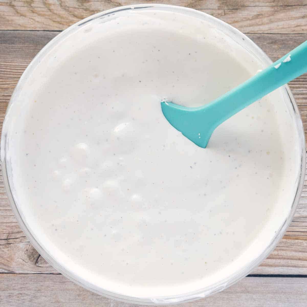 glass bowl of bleu cheese dressing with a blue rubber spatula in the bowl