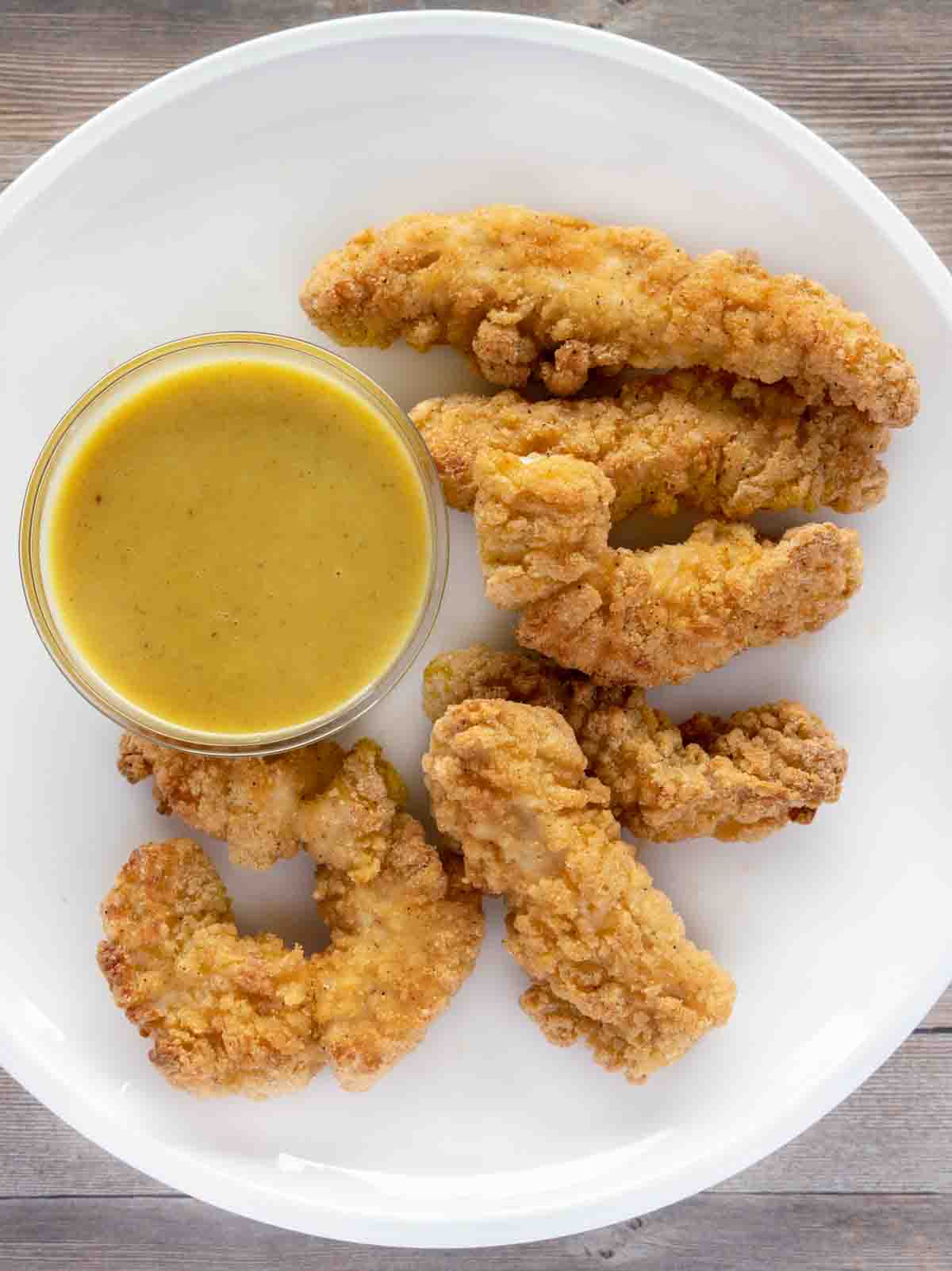 chicken tenders with honey mustard sauce on a white plate.