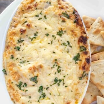 hot crab dip in casserole dish with pita chips on a white plate