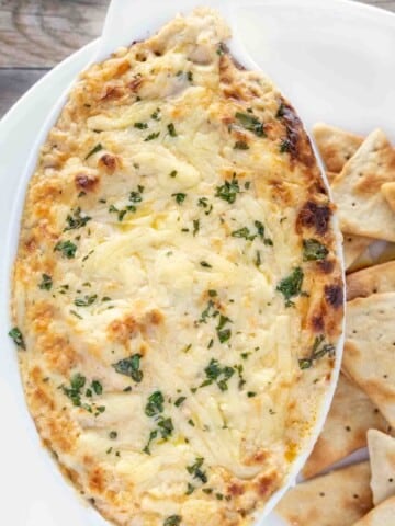 hot crab dip in casserole dish with pita chips on a white plate