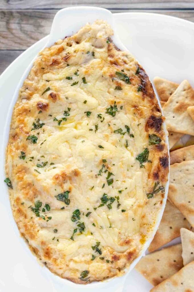 hot crab dip in casserole dish with pita chips on a white plate