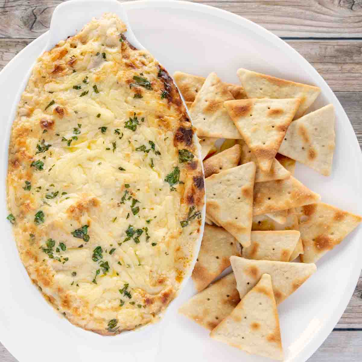 hot crab dip in casserole dish with pita chips on a white plate