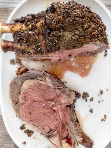 cut of rare prime rib next to roast on white platter