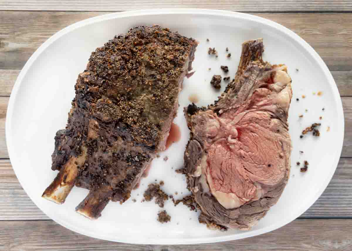 Cooked standing rib roast next to some sliced meat on a white platter.