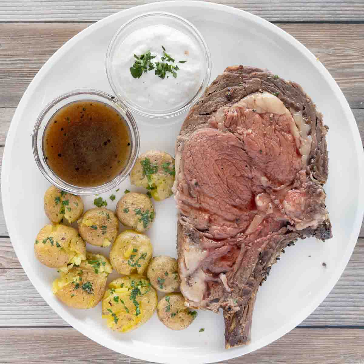 rare prime rib with smashed potatoes, au jus and horseradish sauce on a white plate