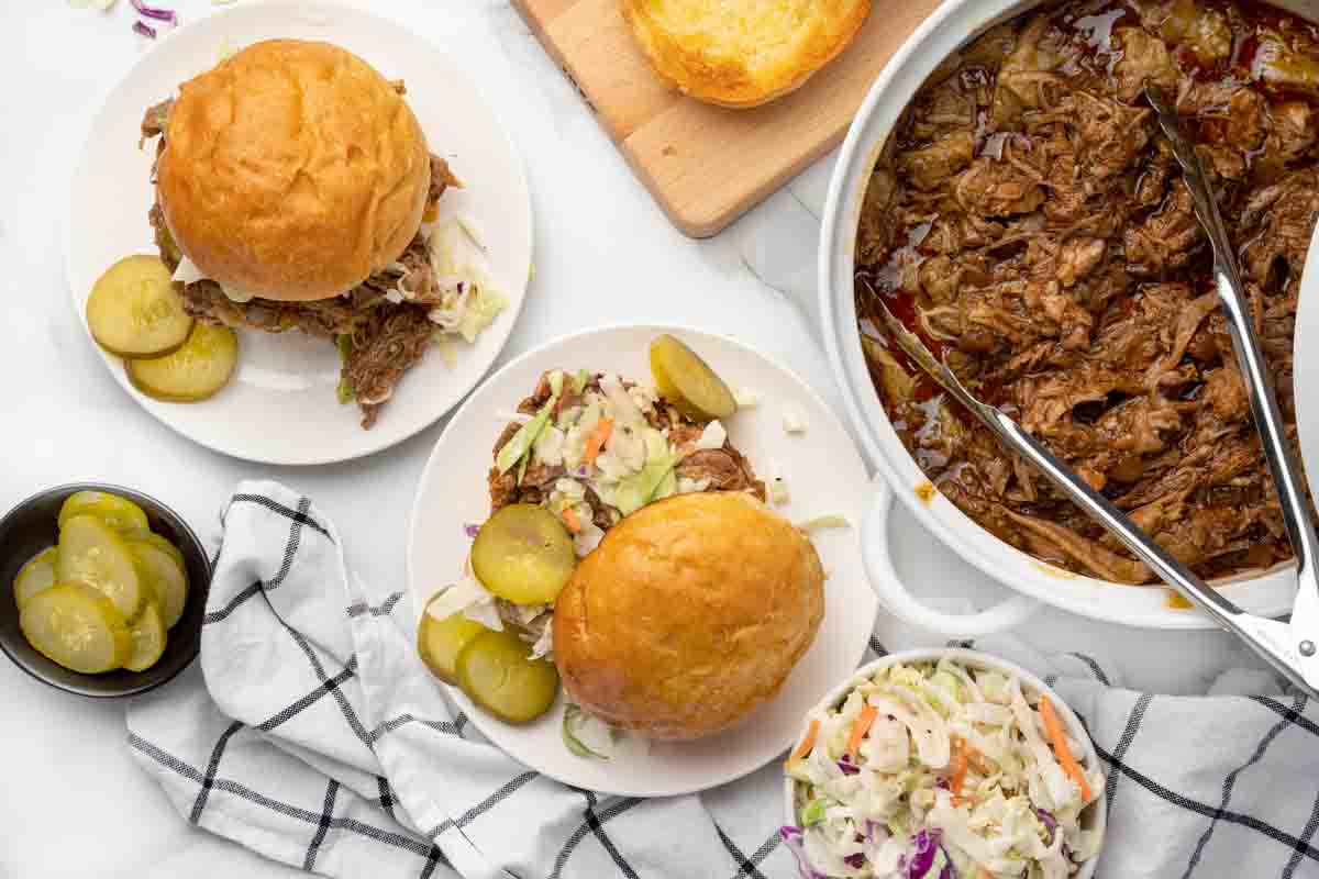 two pork sandwiches next to white pot with barbecue pulled pork