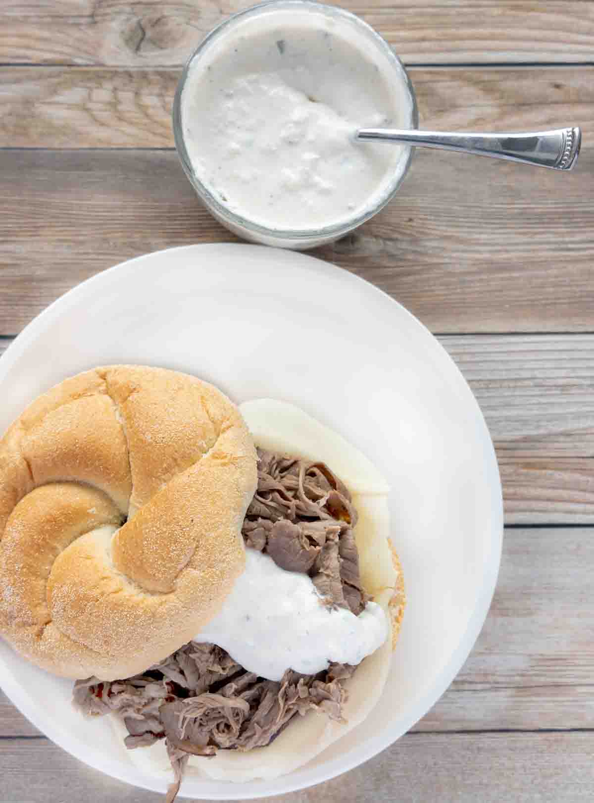 roast beef on kaiser roll with horseradish sauce on white plate