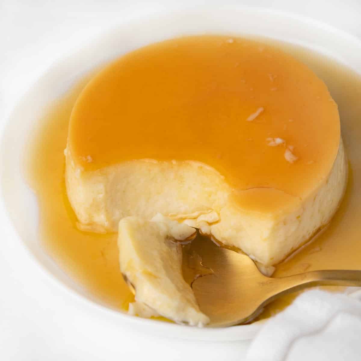 flan on a white plate with a spoon taking a piece out of it