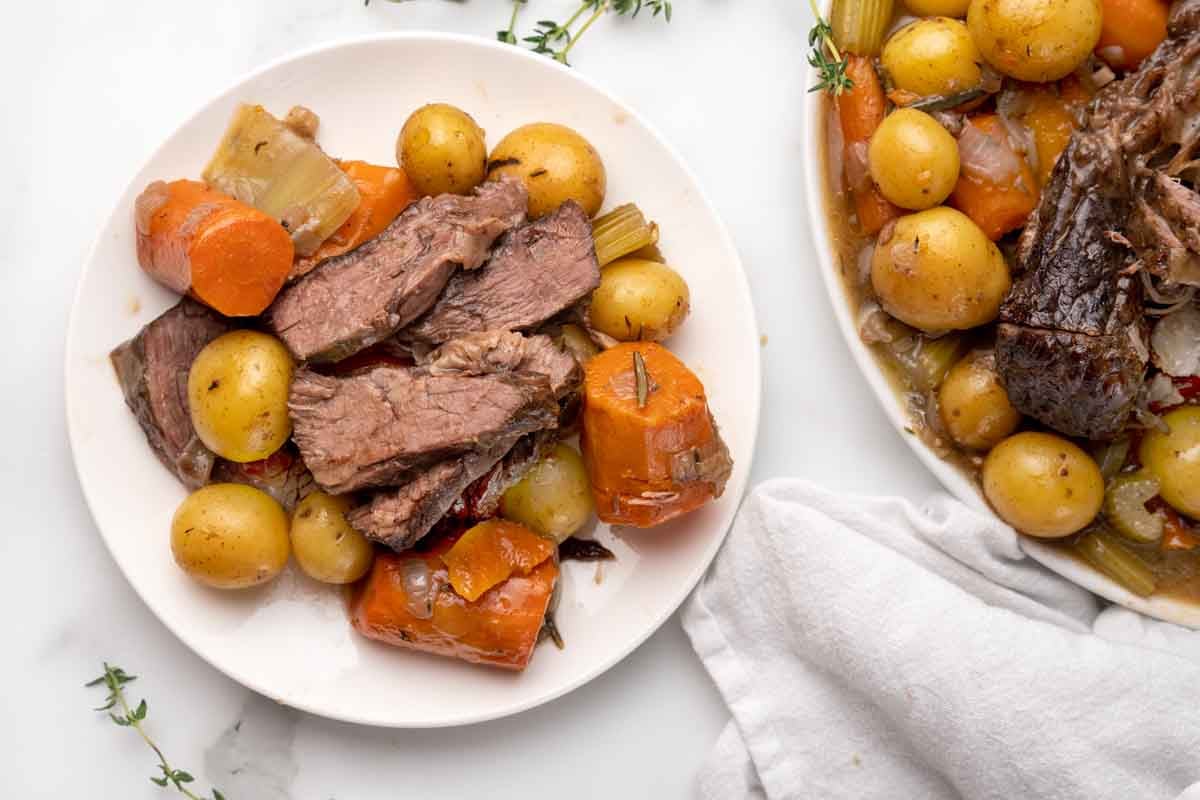 pot roast slices with potatoes and carrots on a white plate.