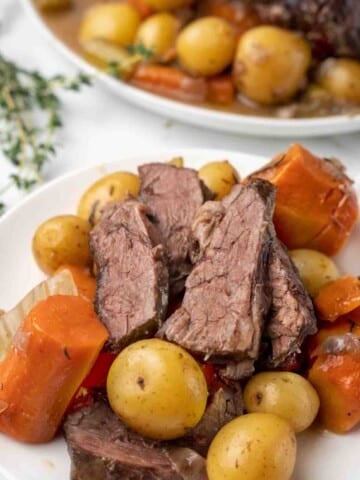 sliced pot roast with potatoes and carrots on a white plate