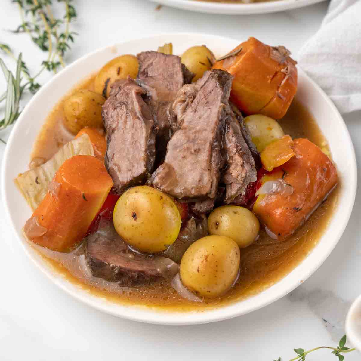 sliced pot roast with carrots and potatoes on a white plate