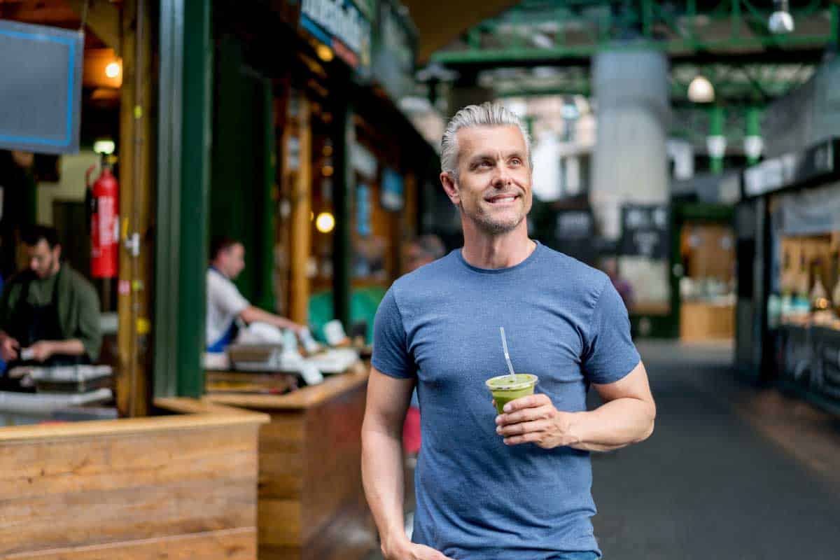 man on street holding a smoothie and smiling