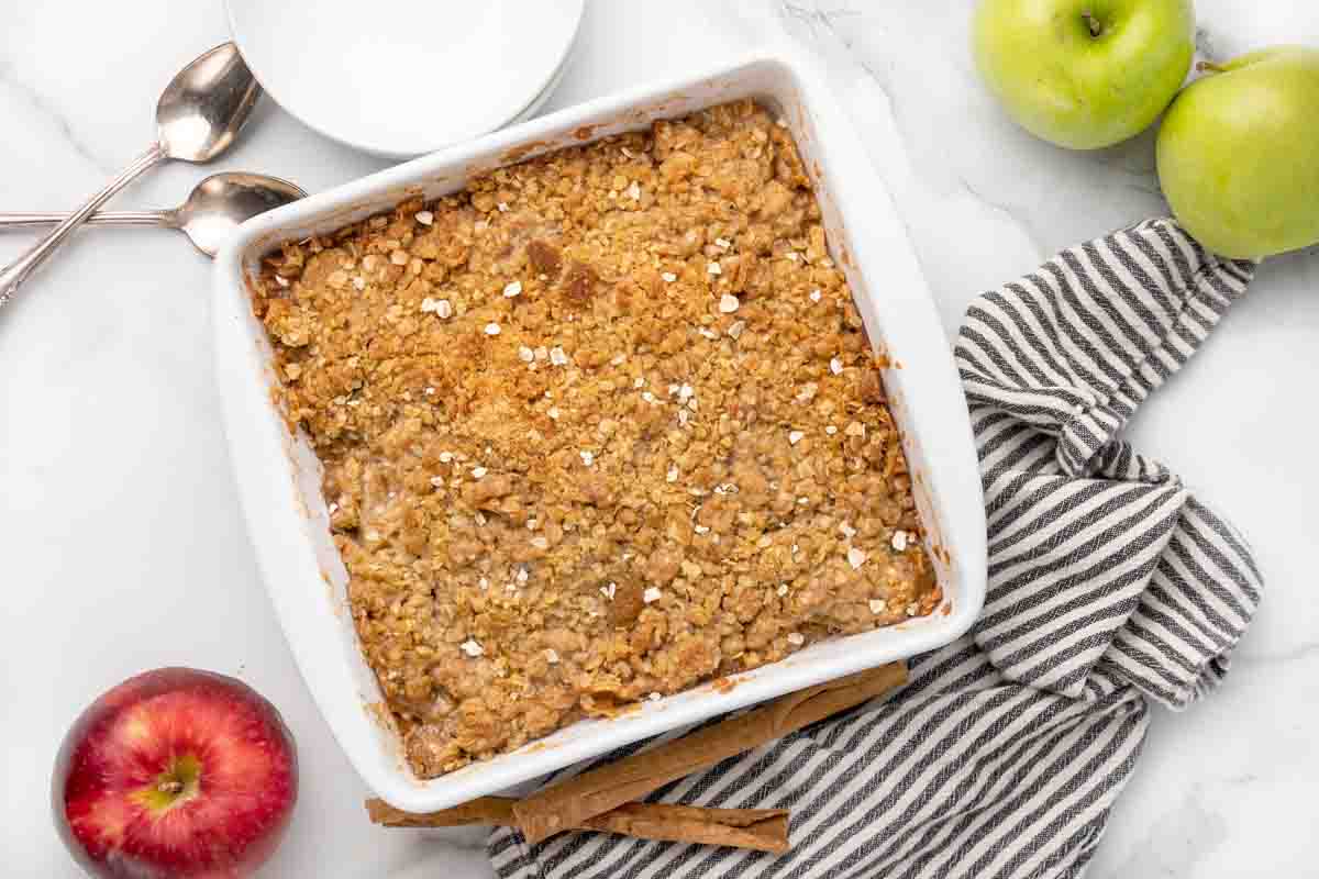 white baking dish with apple crisp next to apples