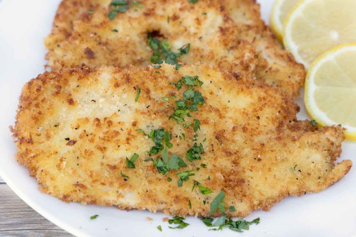 close up of chicken schnitzel on a white plate with lemon circles