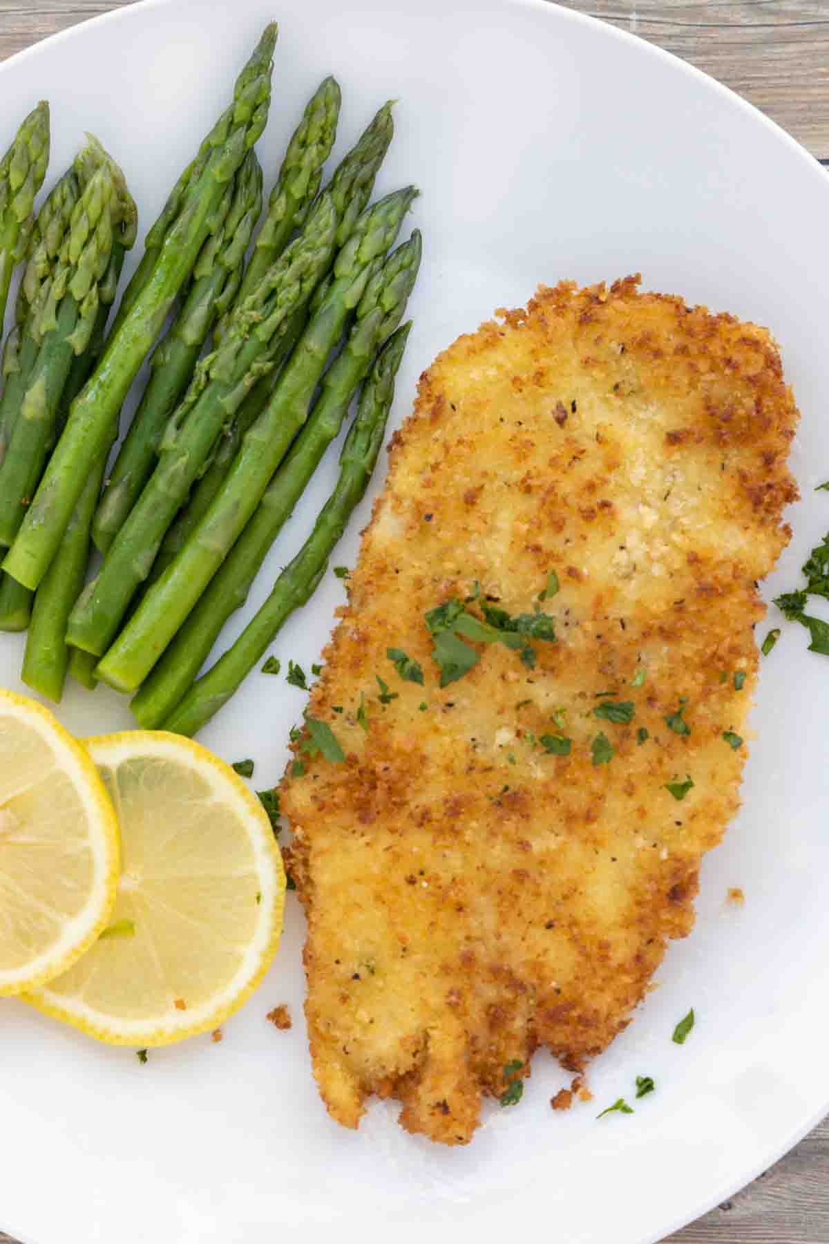 Chicken schnitzel on a white plate with lemon circles and asparagus.