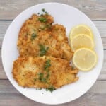 Chicken schnitzel on a white plate with lemon circles.