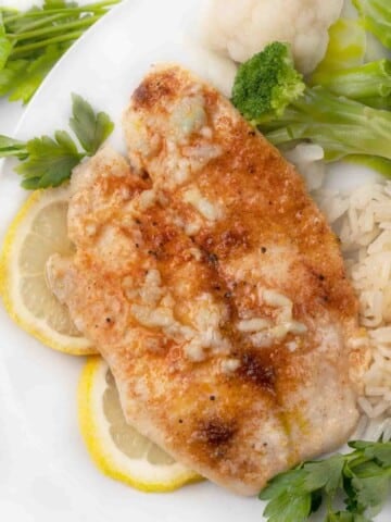 garlic butter tilapia on white plate with lemon circles