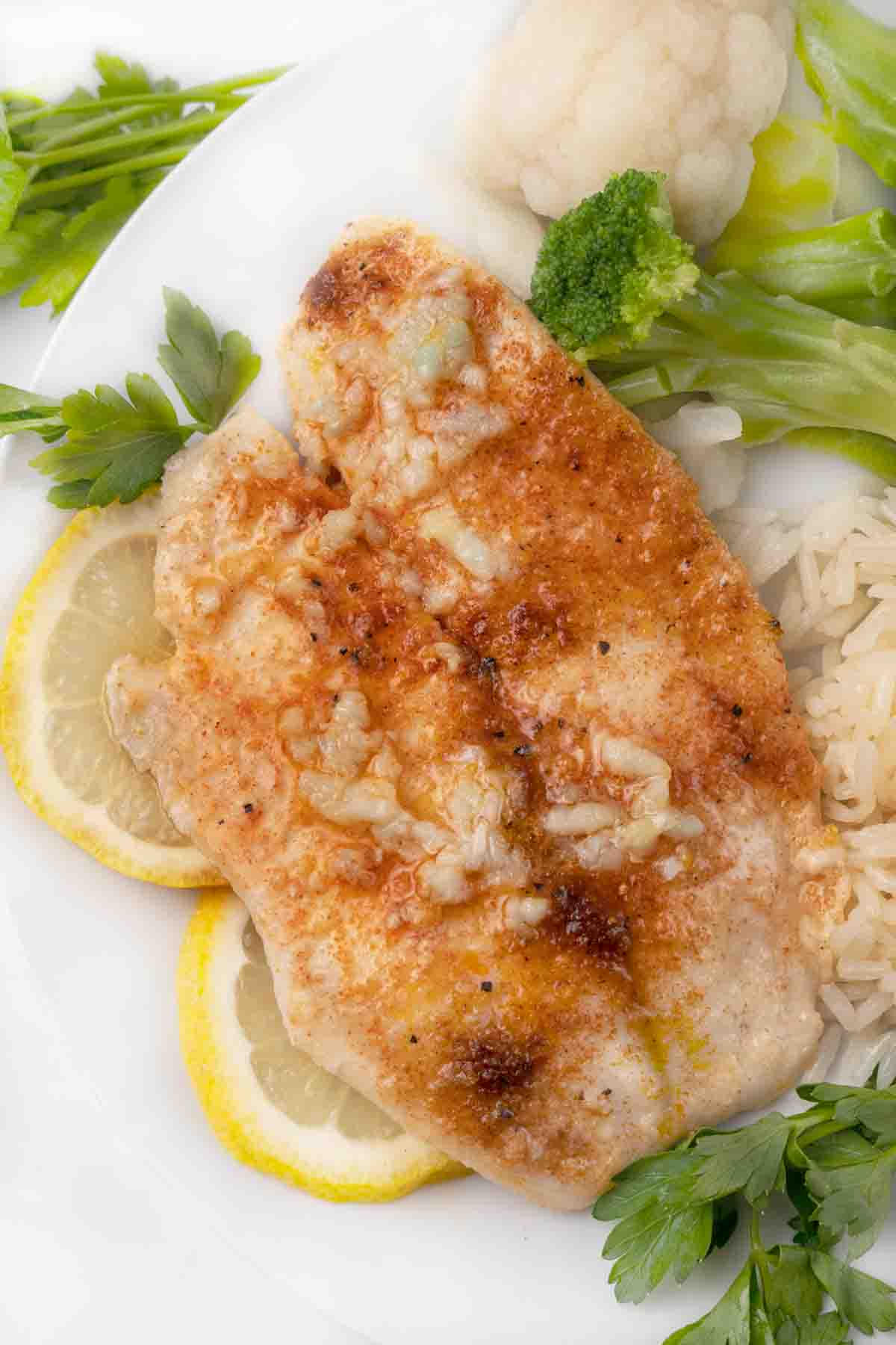 garlic butter tilapia on white plate with lemon circles