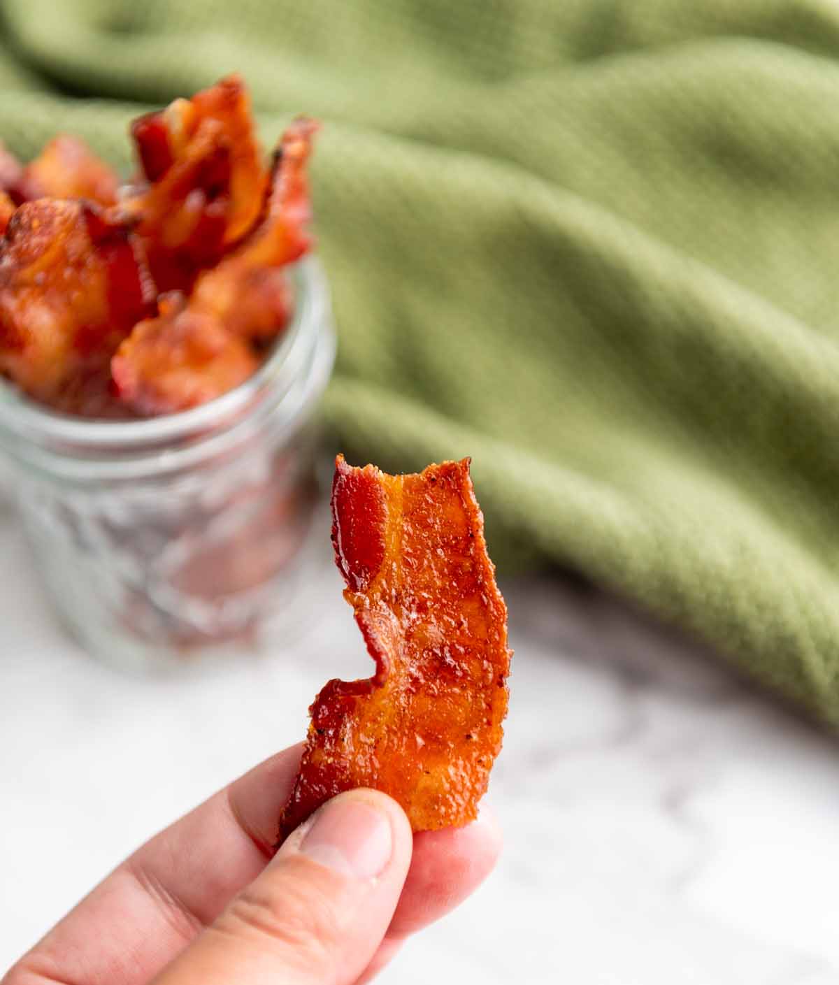 fingers holding piece of candied bacon