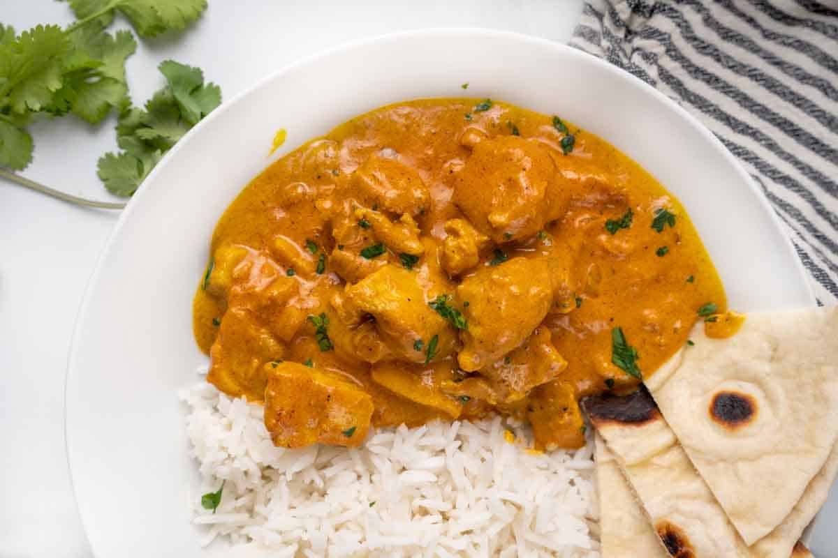 tikka masala with rice and naan bread in a white bowl.