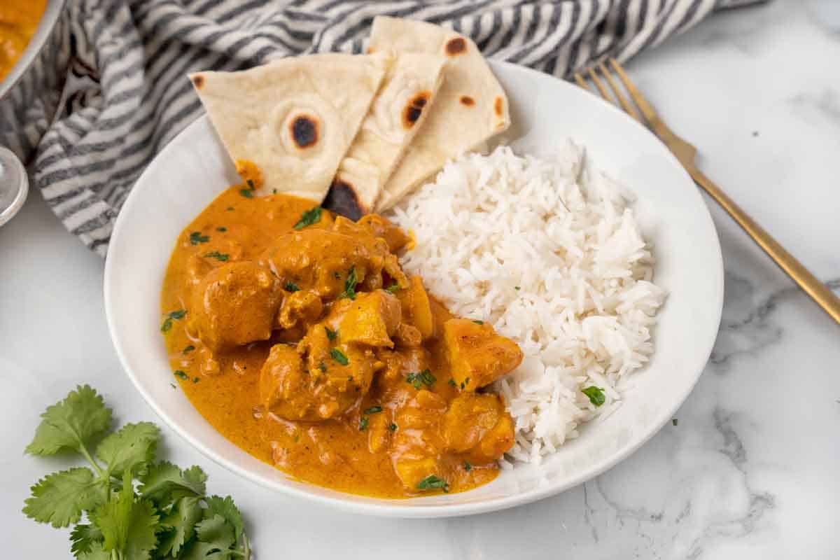 tikka masala with rice and naan bread in a white bowl.
