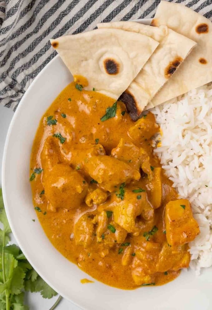 tikka masala with rice and naan bread in a white bowl.