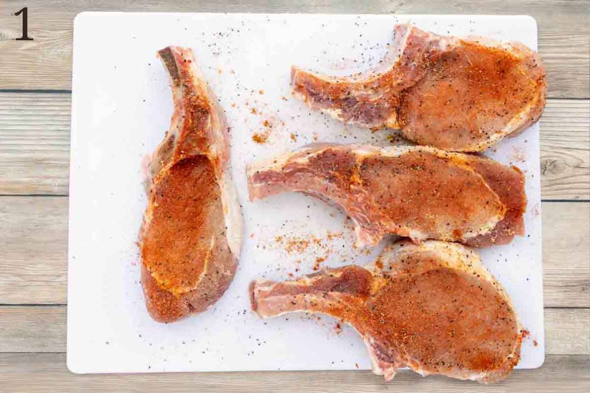 Seasoned pork chops on white cutting board.