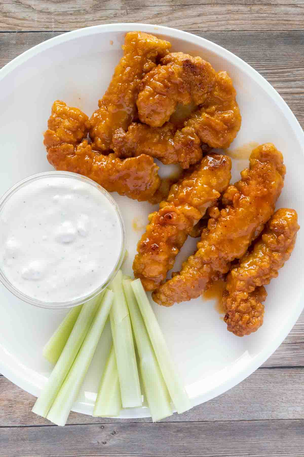 buffalo chicken tenders with bleu cheese and celery on a white plate.