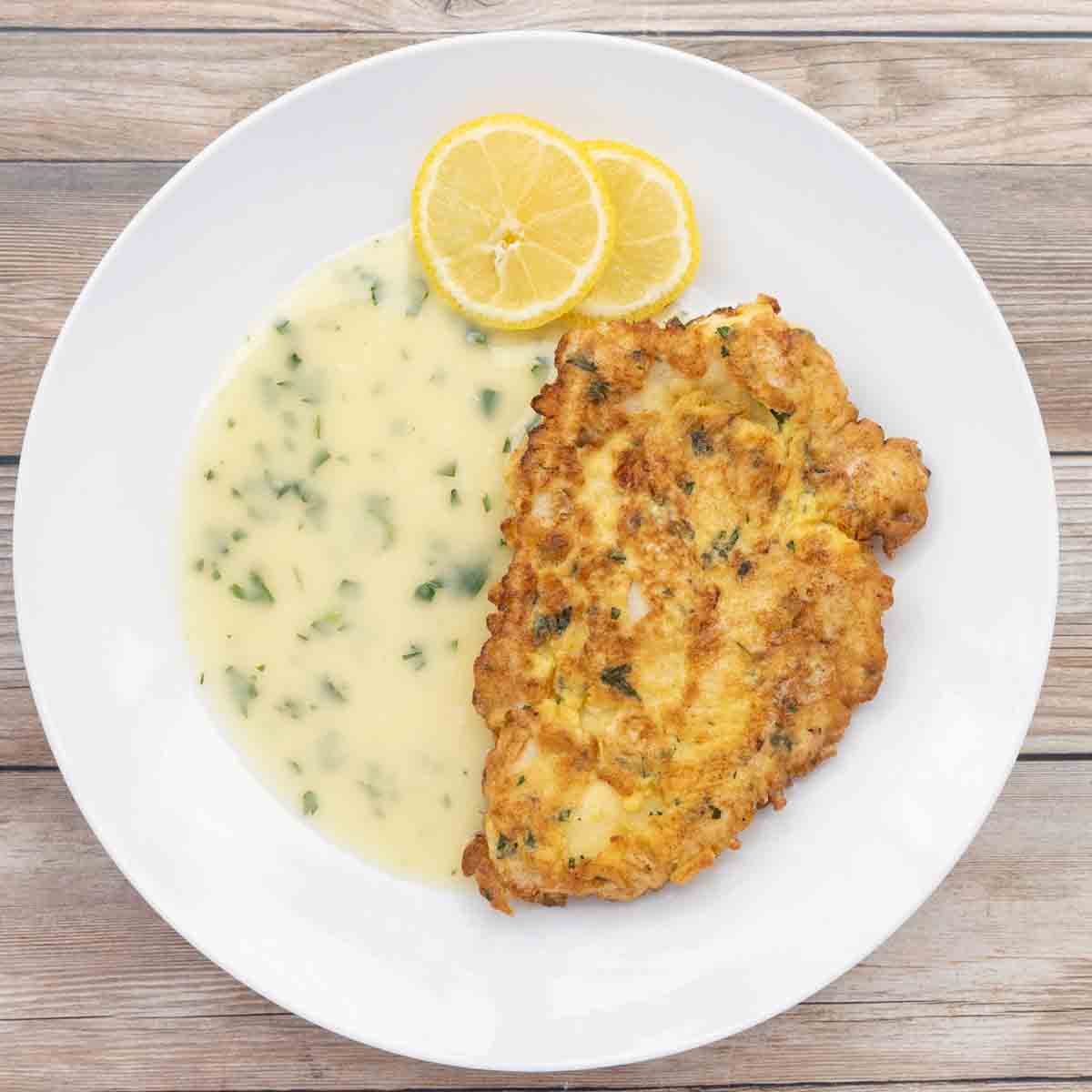 chicken francaise with lemon butter sauce on white plate.