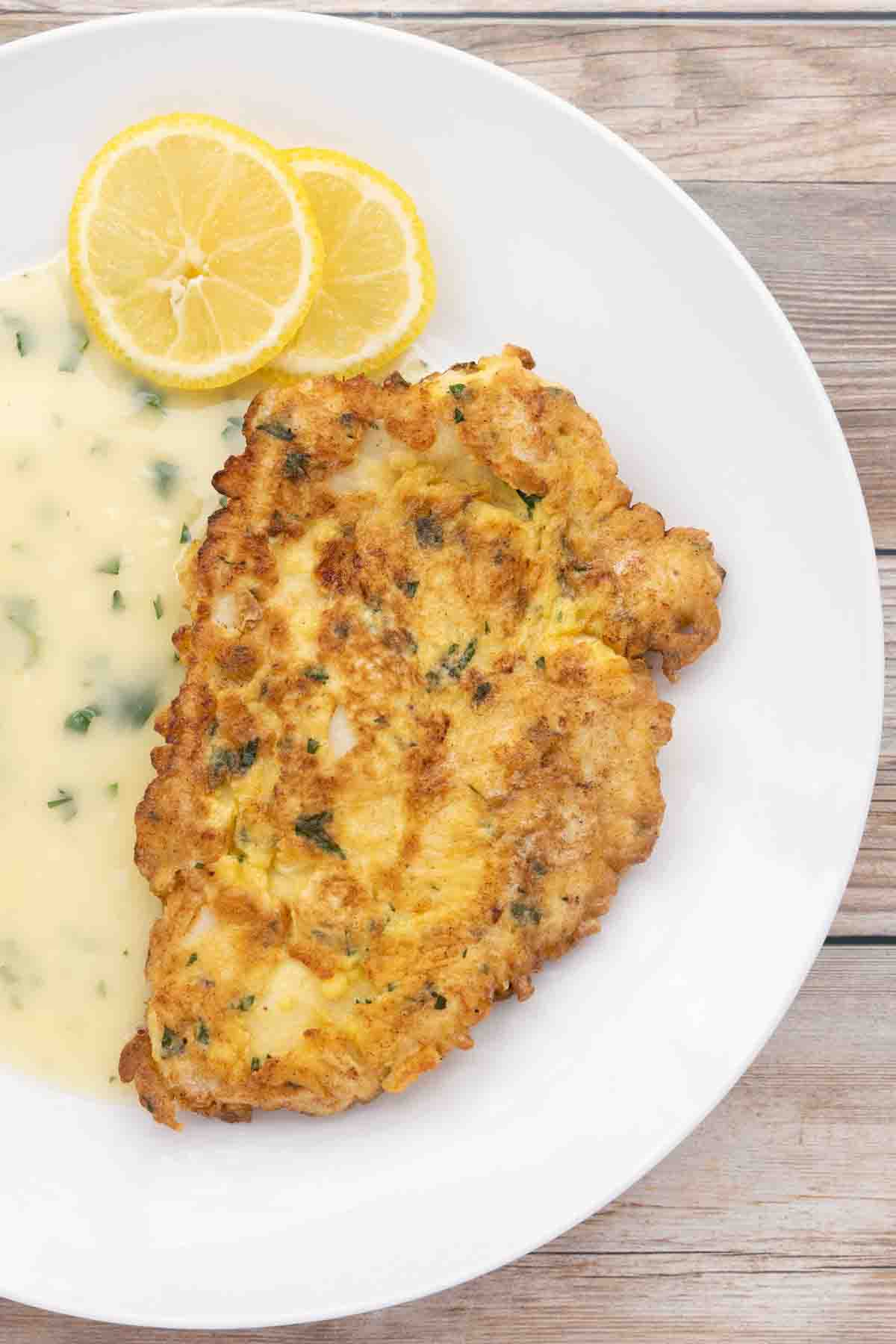 chicken francaise with lemon butter sauce on white plate.