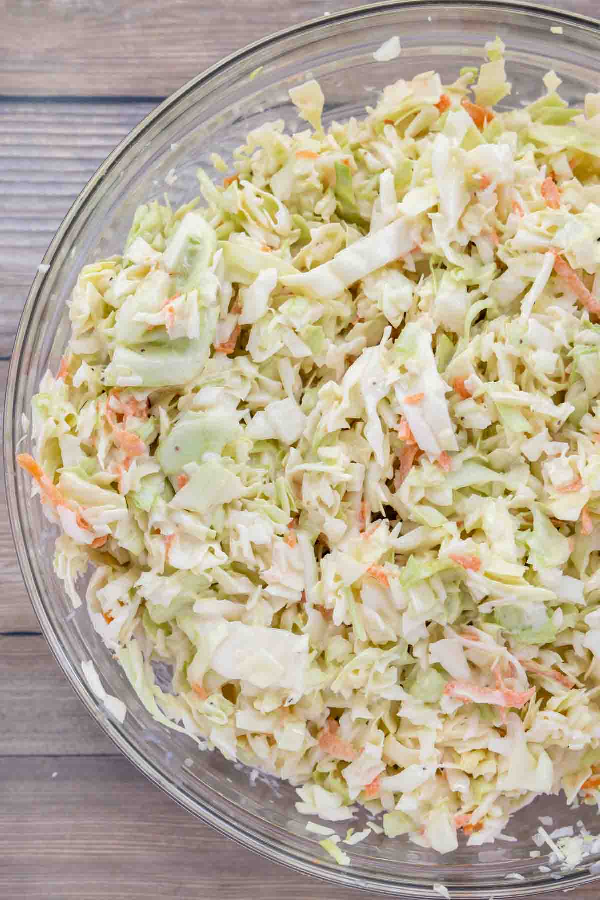 shredded cabbage and carrots mixed with dressing in a glass bowl.