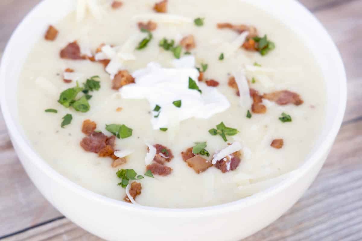 potato soup with bacon bits, sour cream and cheddar cheese topping in a white bowl