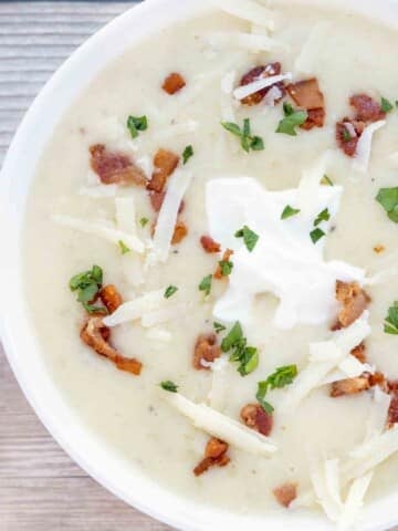 potato soup with bacon bits, sour cream and cheddar cheese topping in a white bowl