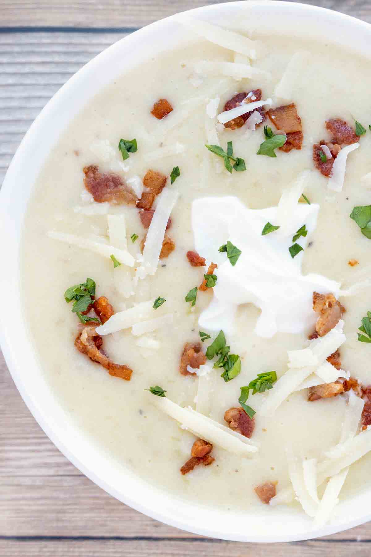 potato soup with bacon bits, sour cream and cheddar cheese topping in a white bowl