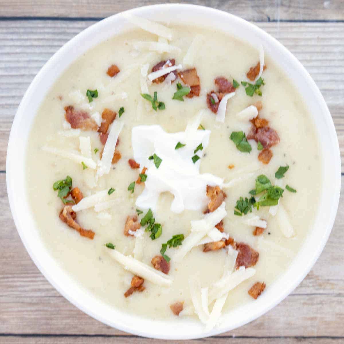 potato soup with bacon bits, sour cream and cheddar cheese topping in a white bowl