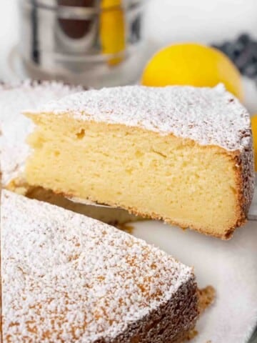 Slice of ricotta lemon cake on a spatula being taken out of whole cake.