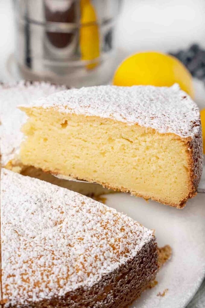 Slice of ricotta lemon cake on a spatula being taken out of whole cake.