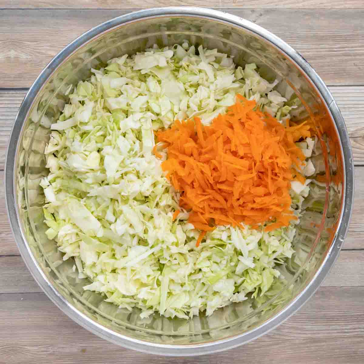 shredded carrots added to bowl of chopped cabbage.