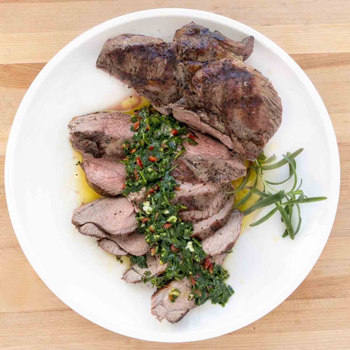 chimichurri sauce served over roast lamb slices on a white plate.