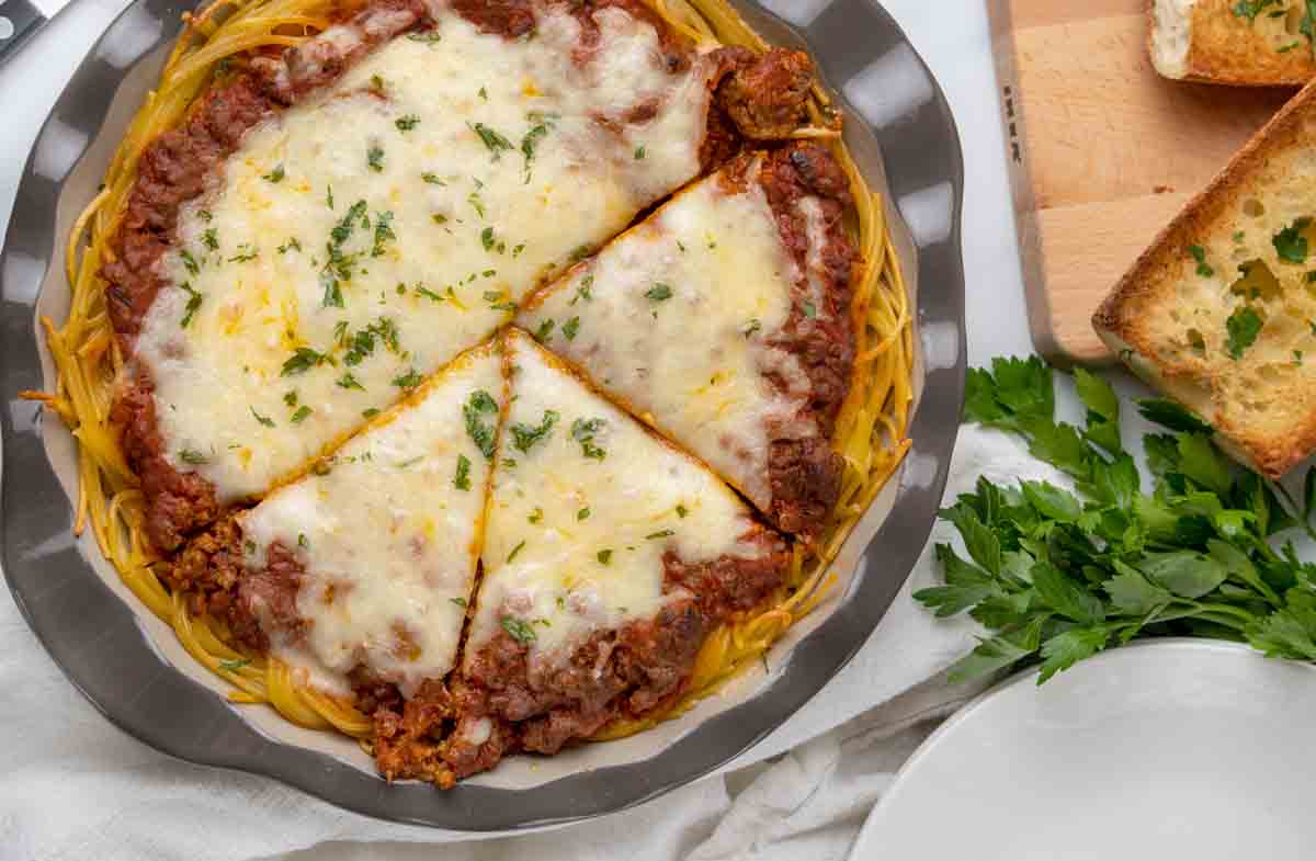 Whole spaghetti pie partially sliced in pie pan.