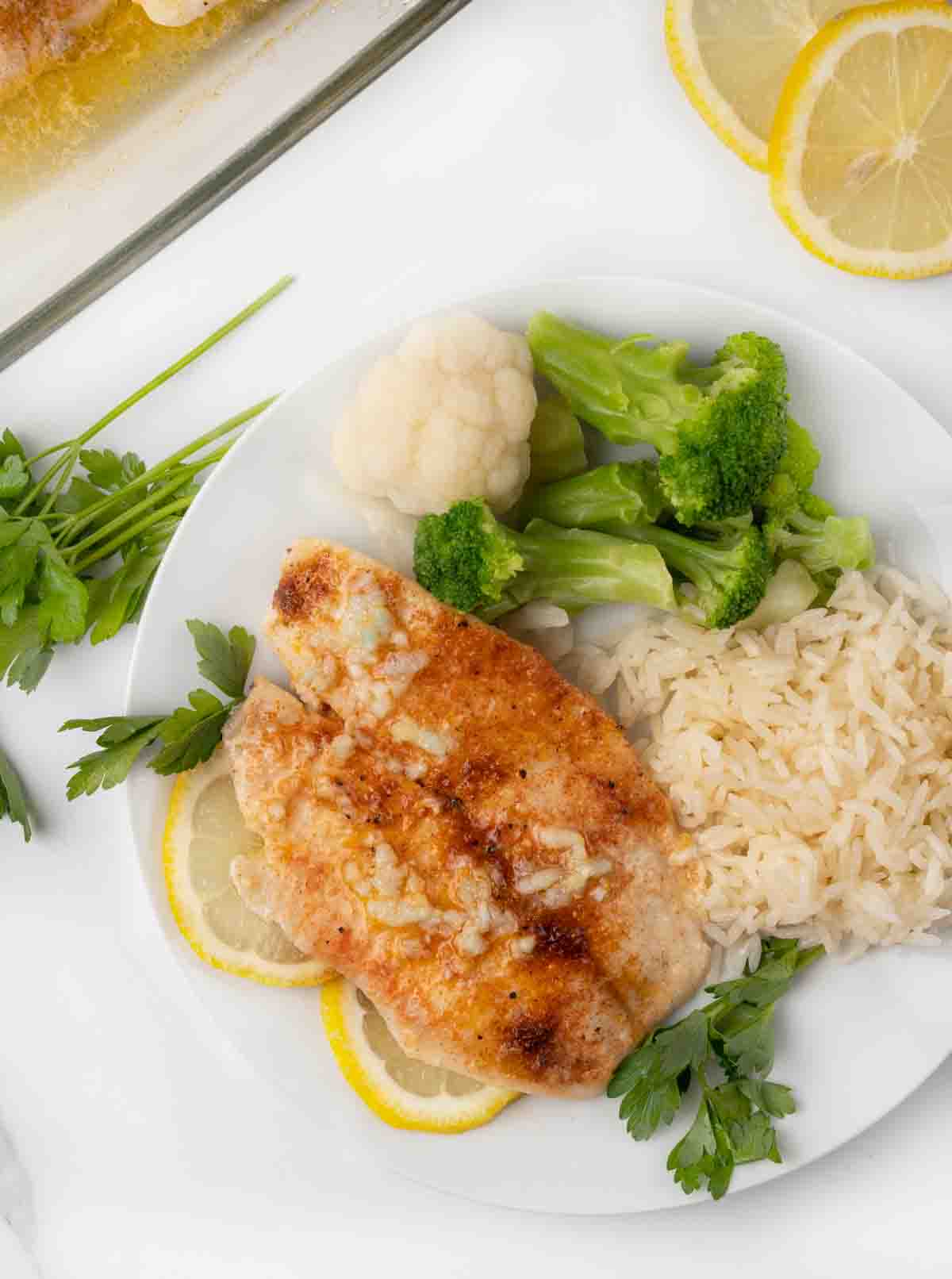garlic butter tilapia on white plate with rice, broccoli and lemon circles